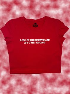 Life Is Dragging Me By The Thong Crop Top - Snug Fit Add a splash of edgy humor to your wardrobe with the "Life Is Dragging Me By The Thong" Crop Top. Whether you're navigating a hectic day or just hanging out with friends, this top is a playful way to express how you're handling the ups and downs of life. You can request a different text color using personalization (shown in second to last slide)! SIZING Please carefully review sizing charts and product descriptions. Due to lighting, phone scre Funny T Shirts For Women, Graphic Crop Tops, Edgy Humor, Funny Crop Tops, Funny Baby Tees, Silly Shirt, Funky Shirts, Y2k Crop Top, Baby Crop Top