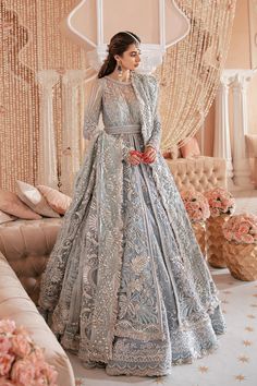 a woman in a blue wedding gown standing next to a couch with flowers on it