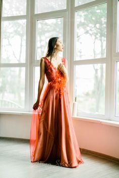 a woman standing in front of a window wearing an orange dress with flowers on it