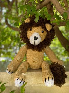 a crocheted lion stuffed animal sitting on top of a tree branch with leaves