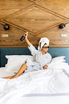 a woman laying on top of a bed with a towel wrapped around her head and holding a hair dryer