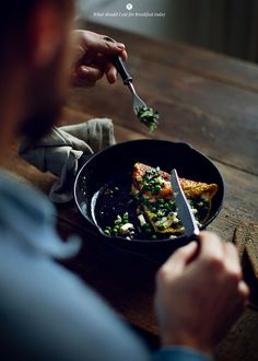 a person is eating food in a skillet on a wooden table with a knife and fork