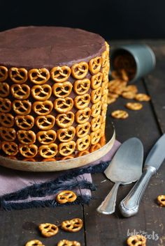 a cake with chocolate frosting and pretzels on top, surrounded by silverware