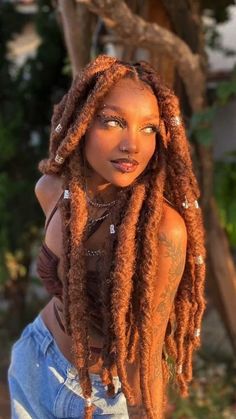 a woman with long dreadlocks standing in front of a tree and looking at the camera