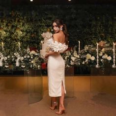 a woman standing in front of flowers wearing a white dress and holding a flower bouquet