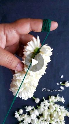 someone is holding some white flowers in their hand and threading them together with green string