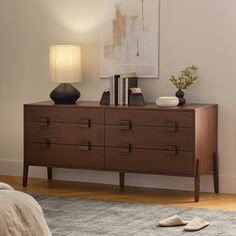 a wooden dresser sitting on top of a carpeted floor next to a lamp and pictures