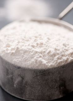 a bowl filled with white powder sitting on top of a black table next to a spoon