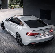 the rear end of a white car parked on a cobblestone street in front of a building