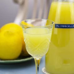 a glass filled with yellow liquid next to lemons on a blue tablecloth and plate