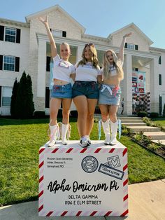 three girls standing on top of a sign in front of a house