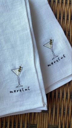 two napkins with embroidered cocktail glasses on them sitting next to each other in front of a wicker basket