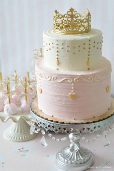 there is a three layer cake with pink frosting and gold decorations on top, along with other desserts