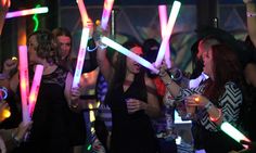 a group of people standing around each other at a party with neon sticks in their hands