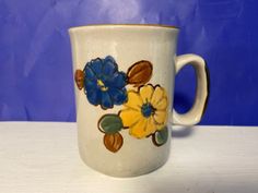 a white coffee cup with blue and yellow flowers painted on the side, sitting on a table