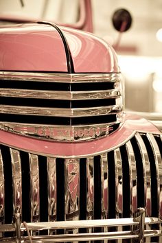 the front end of an old pink and black car with chrome grills on it