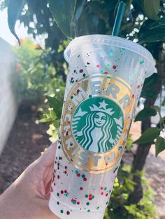 someone holding up a starbucks cup with gold and red sprinkles on it