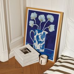 a blue vase with white flowers is on the floor next to books and a cup