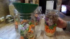 three jars filled with different types of food on top of a wooden table next to a person