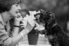 a woman is petting a small black dog on the nose and looking at it