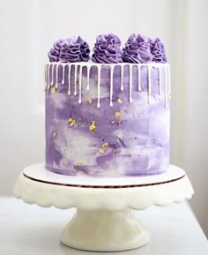 a purple cake with white icing and gold sprinkles sitting on top of a table