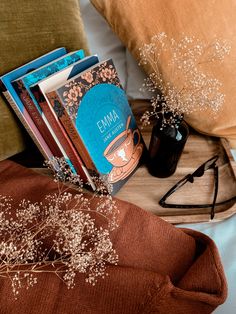 a stack of books sitting on top of a bed next to a vase with baby's breath