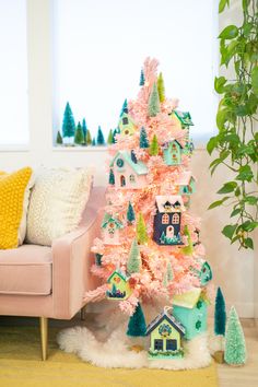 a pink christmas tree with houses and trees on it in front of a couch next to a potted plant