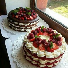 two cakes with strawberries and chocolate frosting sit on a table near a window