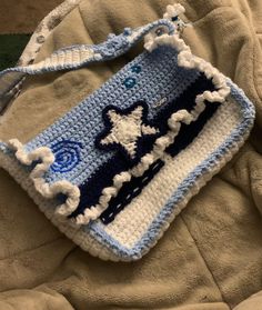 a crocheted blue and white purse with a star on the front is laying on a blanket