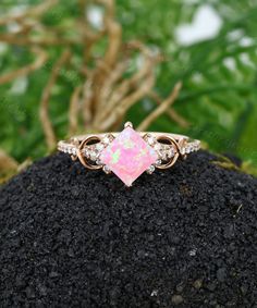 an opal and diamond ring sits on top of a rock in front of some plants