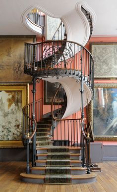 a spiral staircase in the middle of a room with paintings on the wall behind it