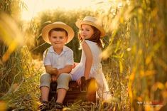 two children sitting on suitcases in the middle of tall grass with sun shining behind them