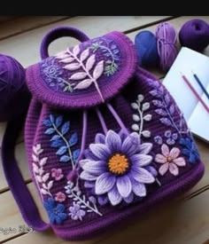 a purple handbag with flowers and leaves on it next to balls of yarn, scissors and knitting needles