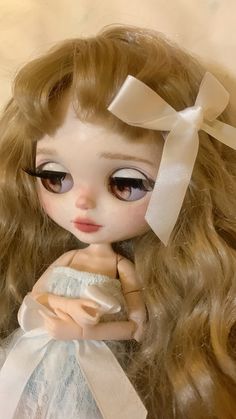 a close up of a doll with long blonde hair and big eyes wearing a white dress