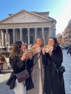 three women eating sandwiches in front of a building