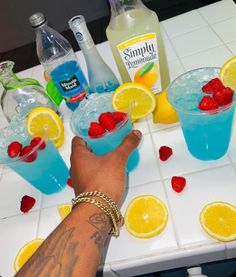 a person's hand reaching for some fruit in two glasses on a table with lemons and raspberries