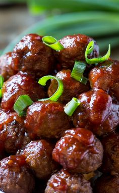 a bowl filled with meatballs covered in sauce and green onions on top of a table