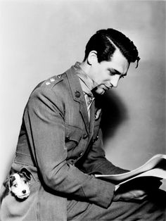 a man in uniform reading a book while sitting on a chair with a stuffed animal