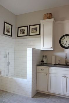 a kitchen with white cabinets and tile flooring next to a clock on the wall