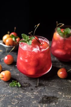 a red drink with mint garnish on the rim surrounded by small oranges