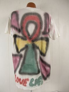 "Vintage 1990s primitive outsider or folk art style t shirt. Made of white cotton with 2 sided air brushed graphics. Has large portrait on the front and symbol on back. Reads: Come back Jesus Love Life. Signed: Loren A. Evans 91. Size extra large. Actual measurements are: 46\" around the chest 46\" around the waist 22\" shoulder seam to shoulder seam 32\" overall length In excellent condition." Bohemian Cotton T-shirt For Streetwear, Vintage Hand Printed Short Sleeve T-shirt, Vintage Hand-printed Short Sleeve T-shirt, Artsy White T-shirt With Artwork, Vintage Cotton T-shirt For Festival, Bohemian Short Sleeve T-shirt For Streetwear, Hand Printed T-shirt For Summer Streetwear, Summer Streetwear Hand Printed T-shirt, Artistic Hand Painted Short Sleeve T-shirt