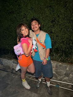 a man and woman standing next to each other in front of a hedge at night