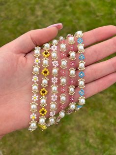 a person's hand holding several bracelets with flowers and pearls on them in the grass