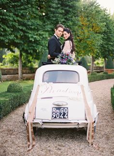 a bride and groom kissing on top of an old car in front of some trees