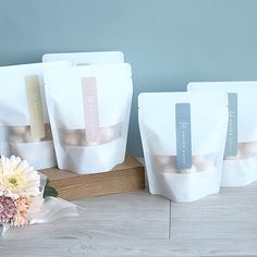 five bags of coffee sitting on top of a wooden table next to a white flower