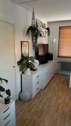 a living room with wooden floors and white furniture, plants on top of the dressers