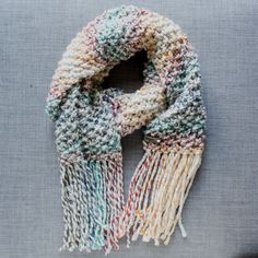 a multicolored knitted scarf with fringes on top of a gray surface