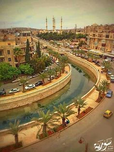 an aerial view of a street with cars driving on the road and buildings in the background