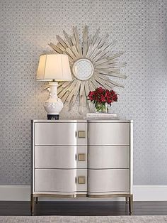 a white dresser sitting next to a lamp on top of a wooden floor in front of a wall