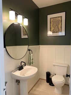 a white toilet sitting next to a bathroom sink under a round mirror in a bathroom